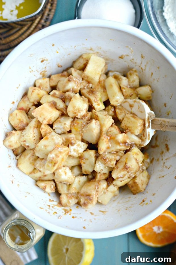 Hands tossing diced apples and pears with brown sugar, spices, and citrus zest in a large mixing bowl
