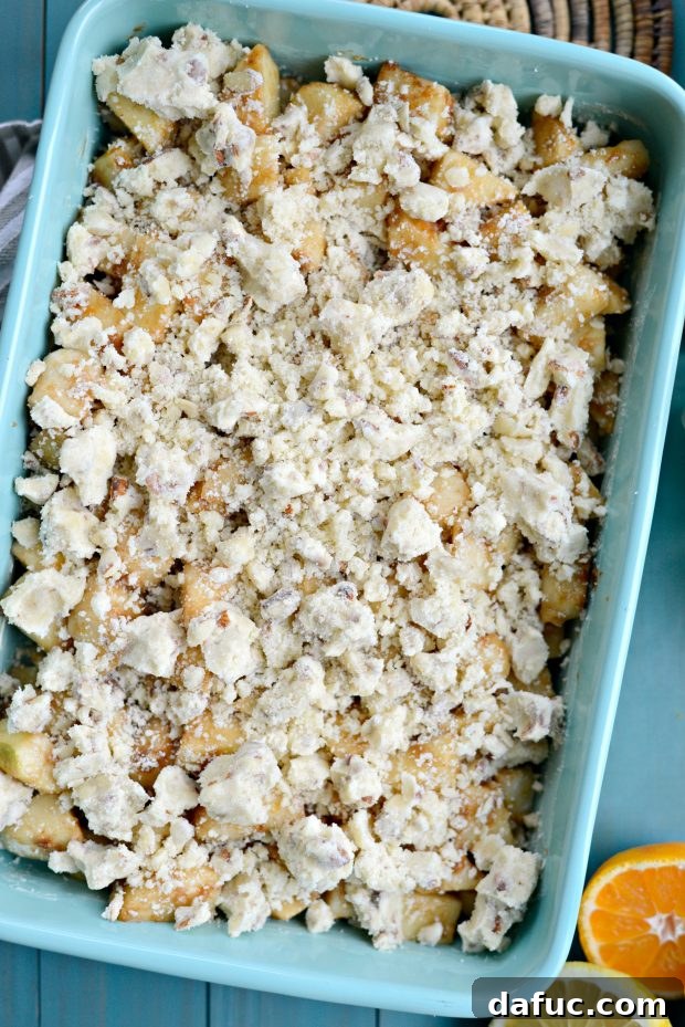 Hands scattering a generous layer of crumble topping over the apple and pear fruit filling