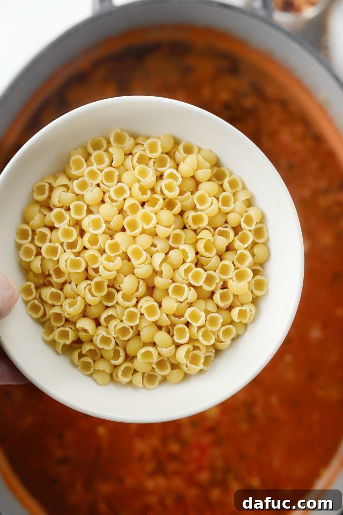 Uncovering the soup and adding tiny pasta shells to cook