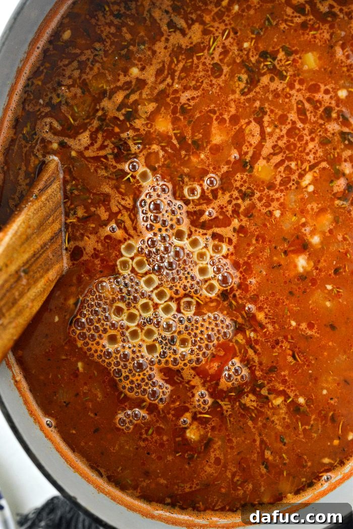 Stirring and simmering the soup with pasta until the pasta is cooked through