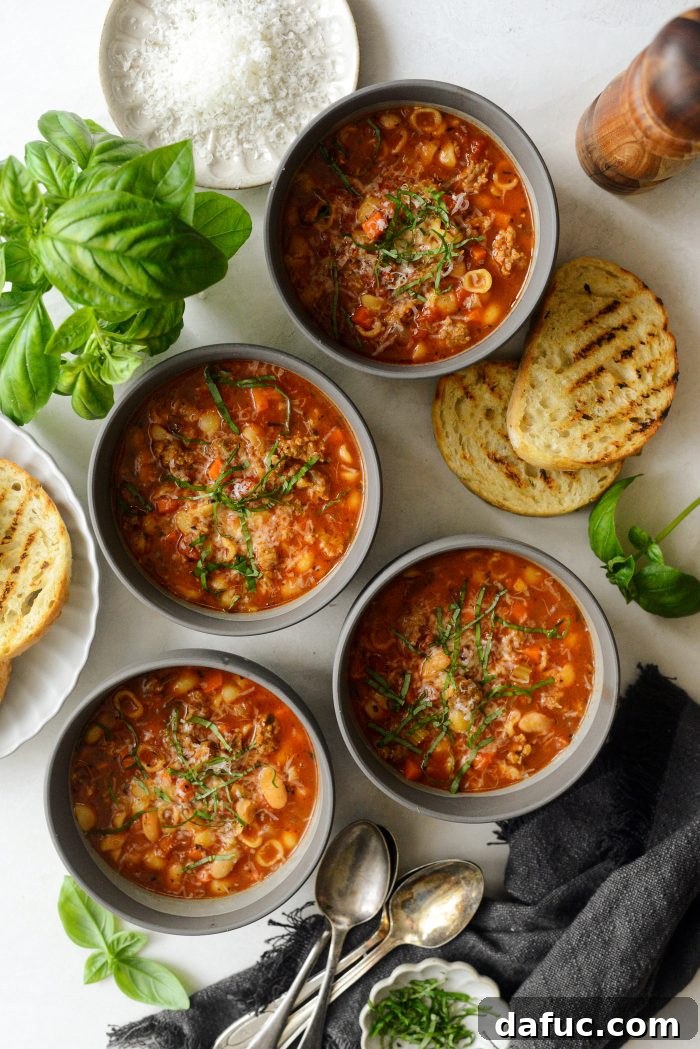 A bowl of Italian Sausage White Bean Soup garnished with fresh herbs and grated Parmesan cheese