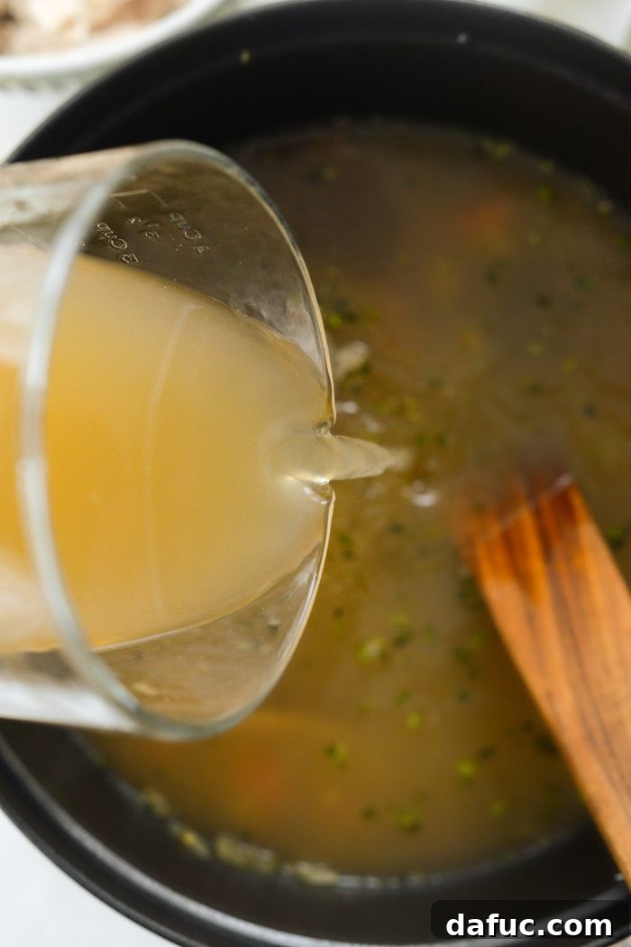 Bright Lemon Rosemary Chicken Noodle Soup 10 Pouring chicken broth into the Dutch oven with vegetables and herbs