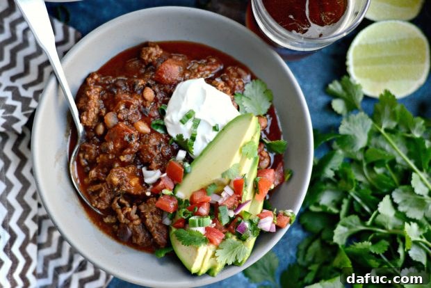 A large pot of steaming Ancho Chorizo Chili garnished with fresh ingredients, ready to be served.