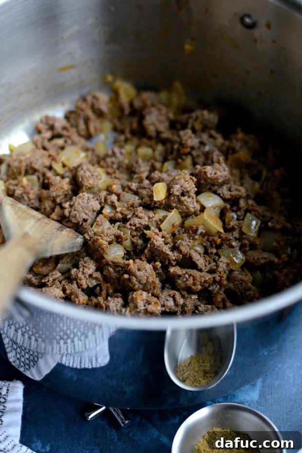 Ground beef and chorizo browning together in a pot, being broken up by a wooden spatula for chili preparation.