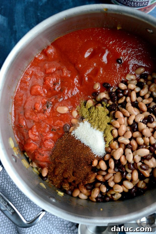 Various canned ingredients, including fire-roasted tomatoes, tomato puree, and beans, being added to the browned meat and onions.