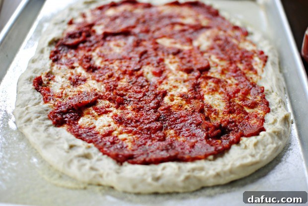 Roasted red pepper pizza sauce being spread onto fresh pizza dough