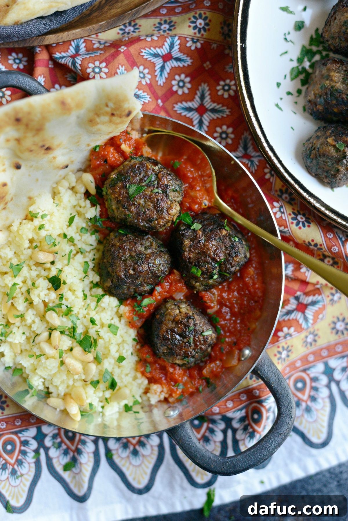 Platter of perfectly browned North African Spiced Lamb Meatballs with a side of red pepper harissa, couscous, and naan.