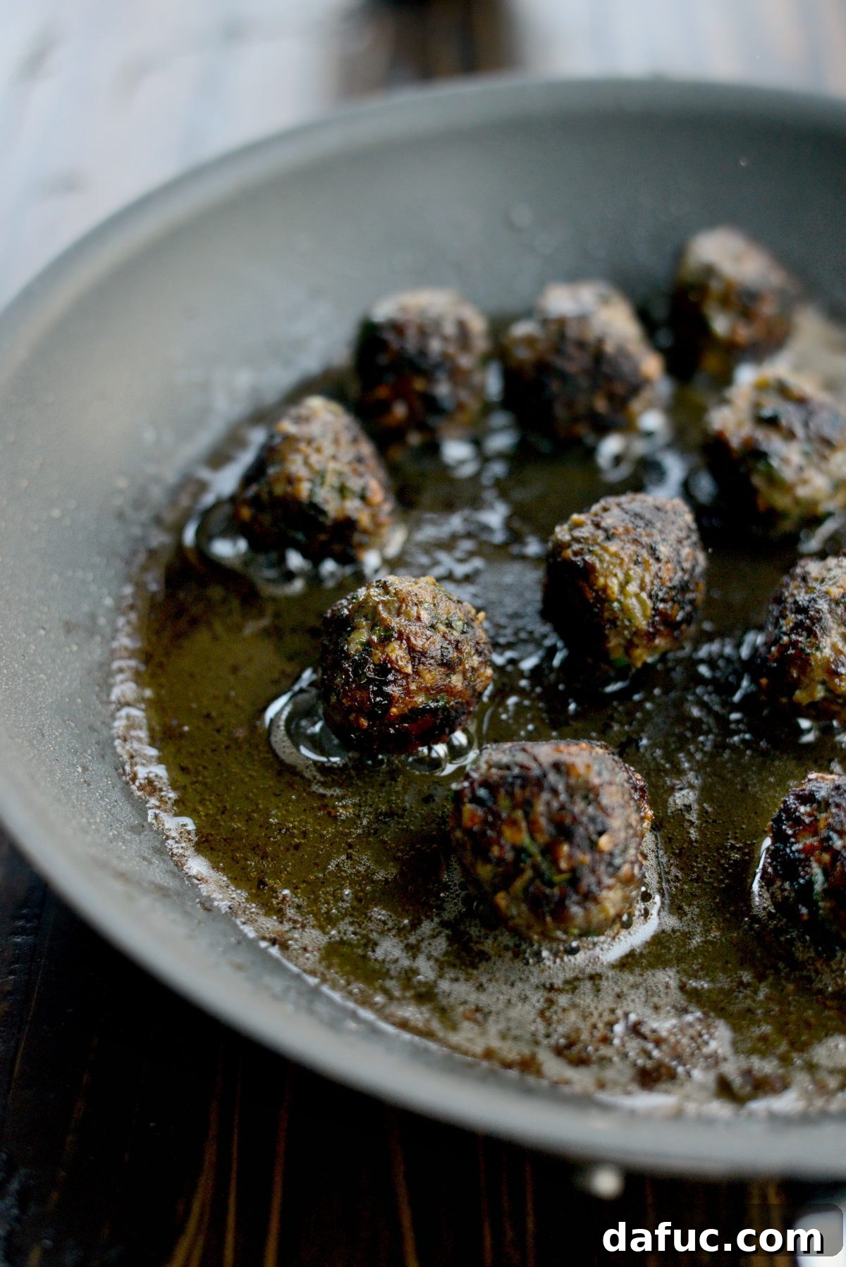 Spiced lamb meatballs browning in a hot skillet with olive oil.