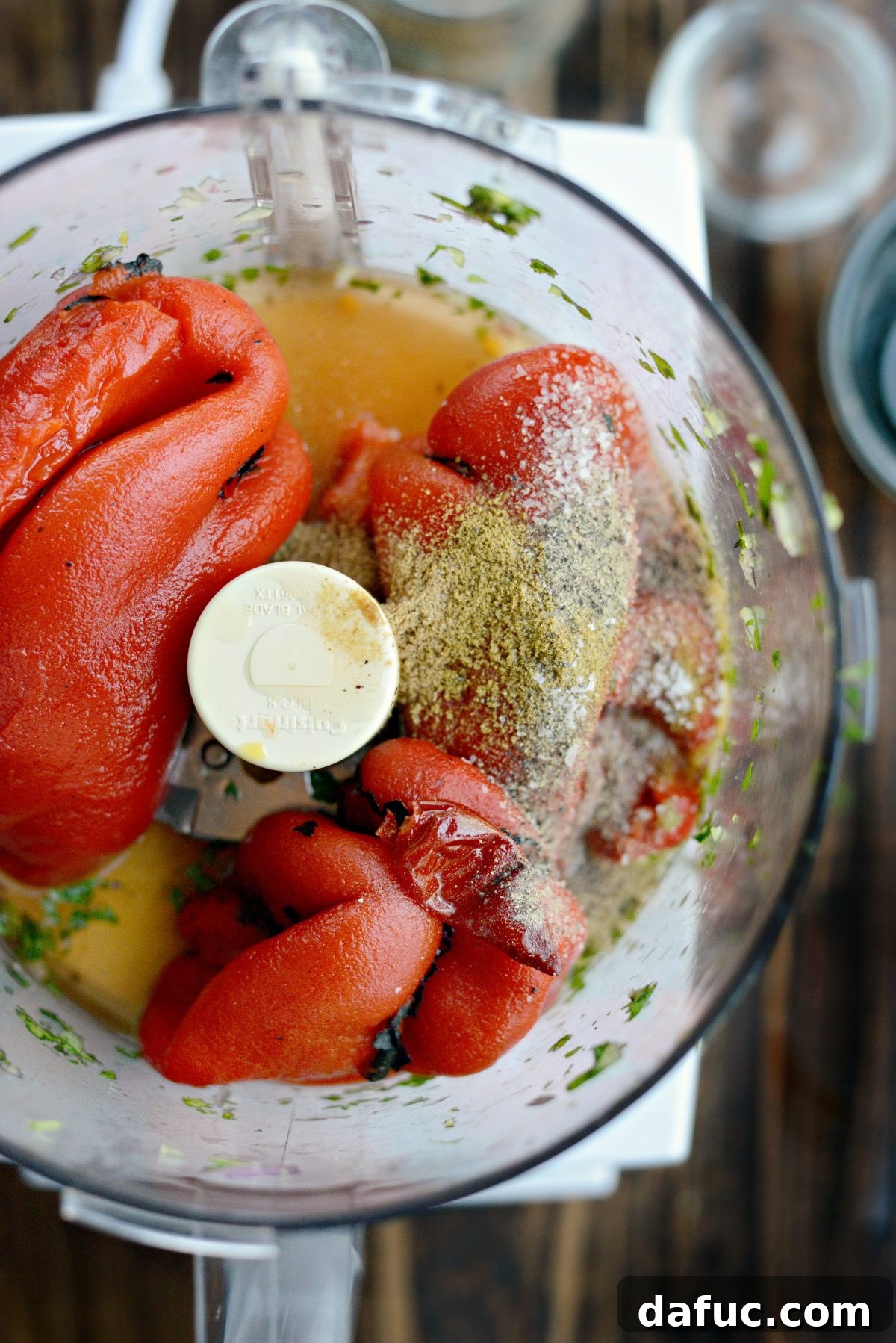 Ingredients for harissa sauce, including roasted red peppers and chili, being added to a food processor.