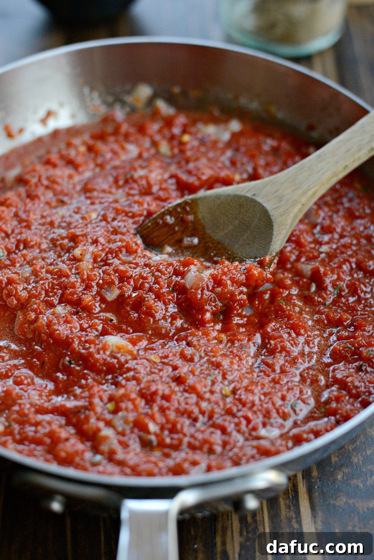 Roasted red pepper harissa sauce poured into a skillet with sautéed onions and garlic, ready to simmer.