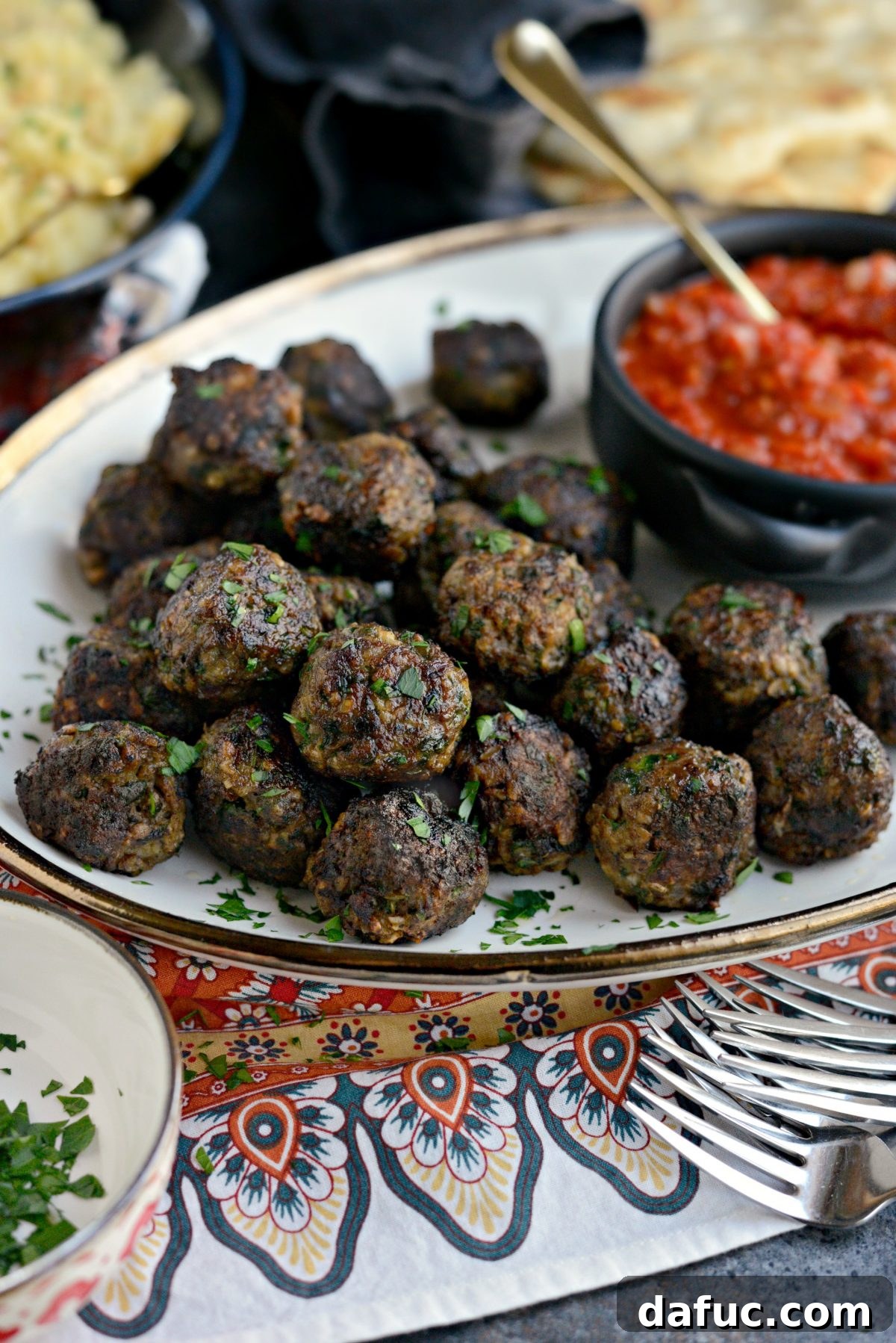 Close-up of North African Spiced Lamb Meatballs on a serving platter with generous dollops of red pepper harissa.