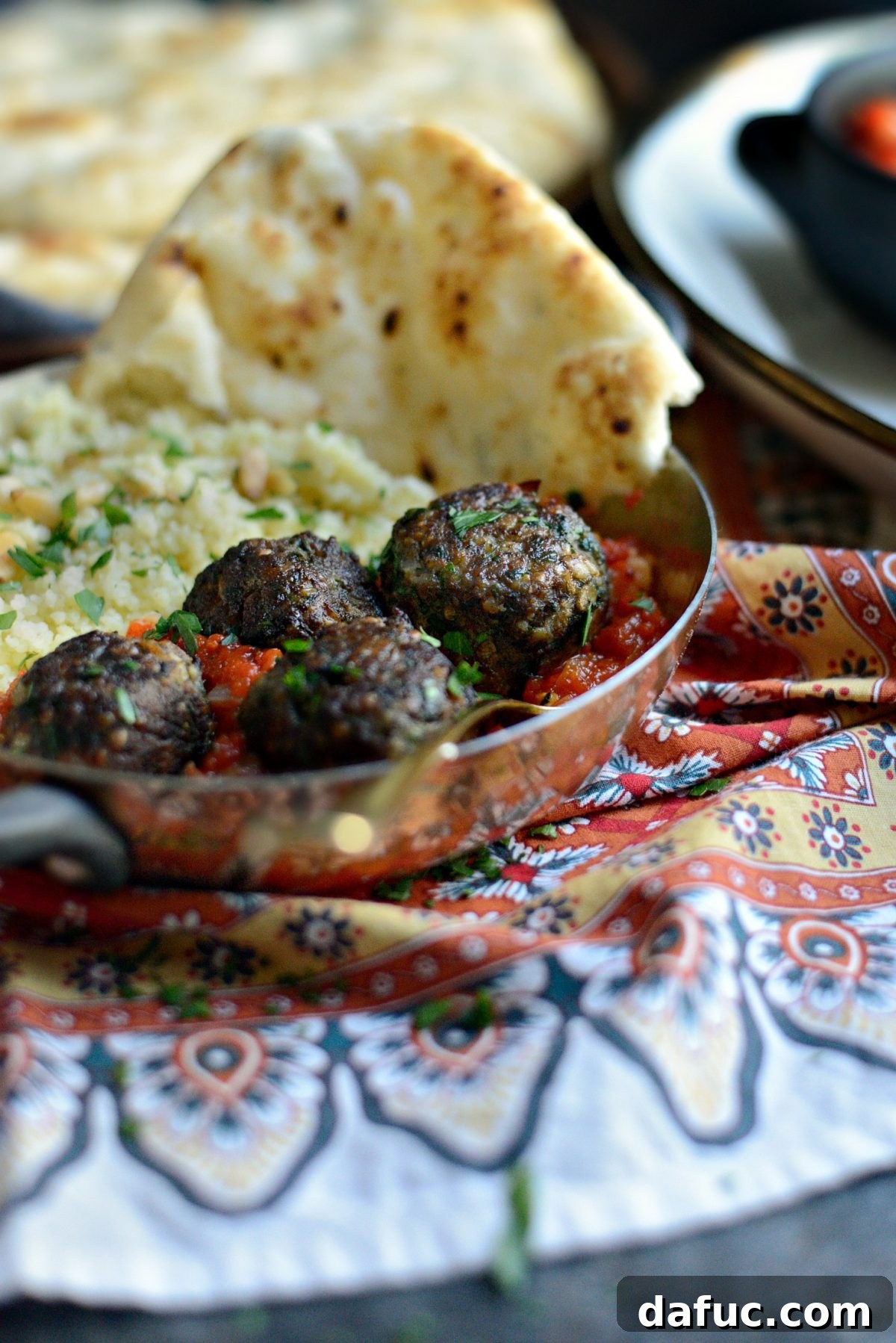 An overhead shot of North African Spiced Lamb Meatballs artfully arranged on a plate with vibrant harissa sauce and fresh herbs.