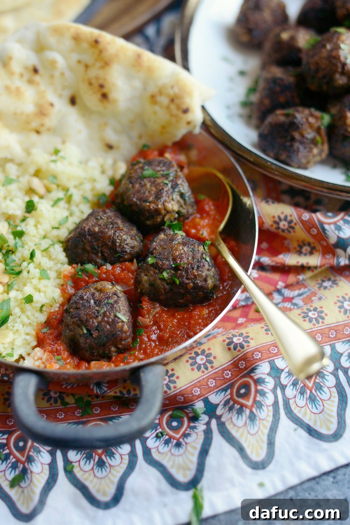 Close-up of a single North African Spiced Lamb Meatball on a fork, showing its juicy texture and seasoning.