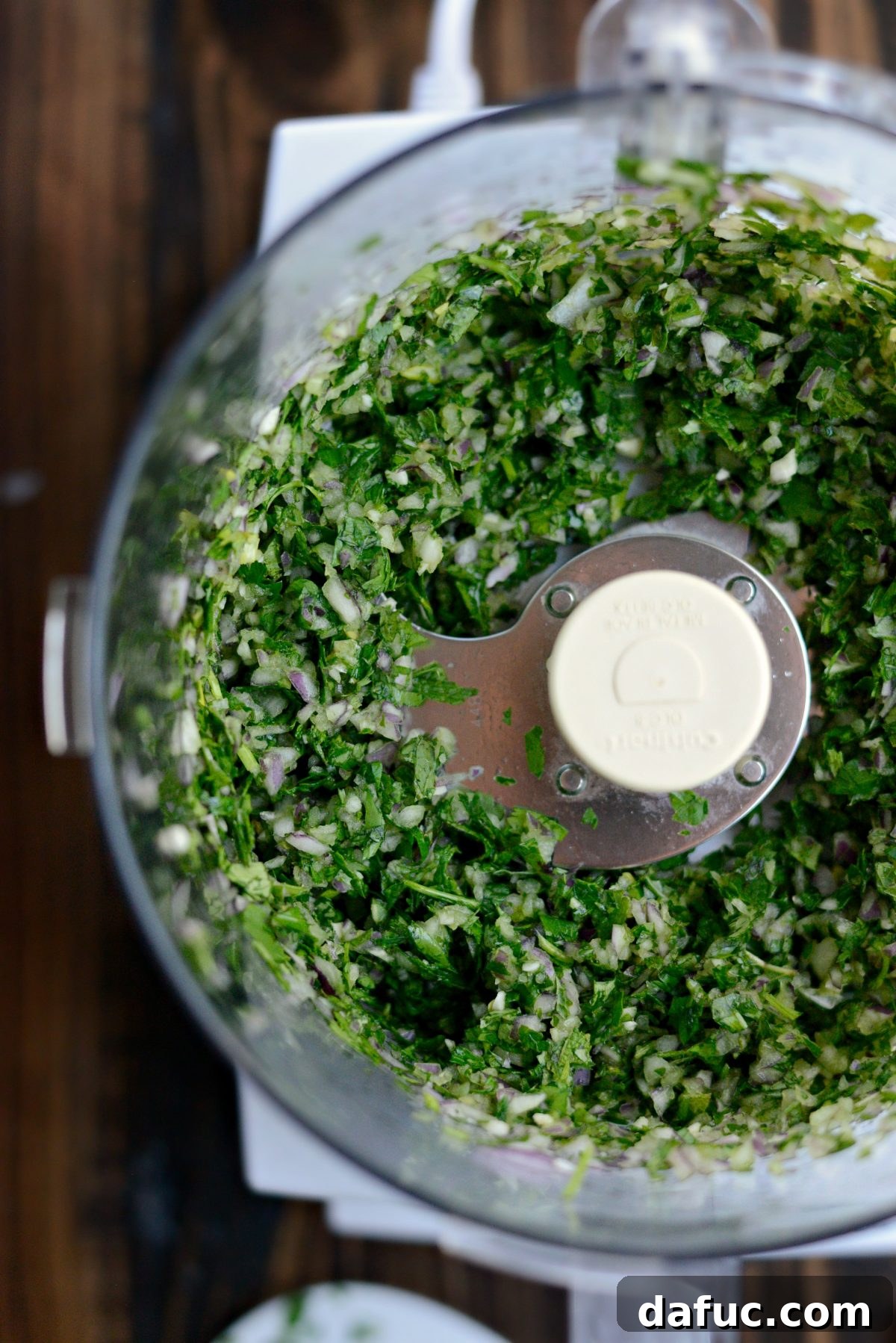 Finely chopped herbs, red onion, and garlic mixture in a food processor bowl.