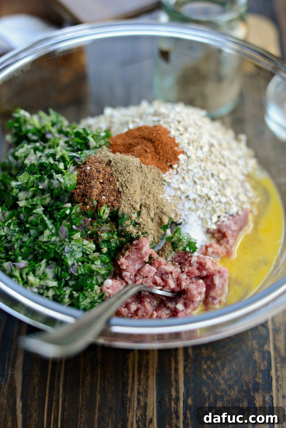 Ground lamb, herb-onion mixture, and spices being combined in a large mixing bowl.