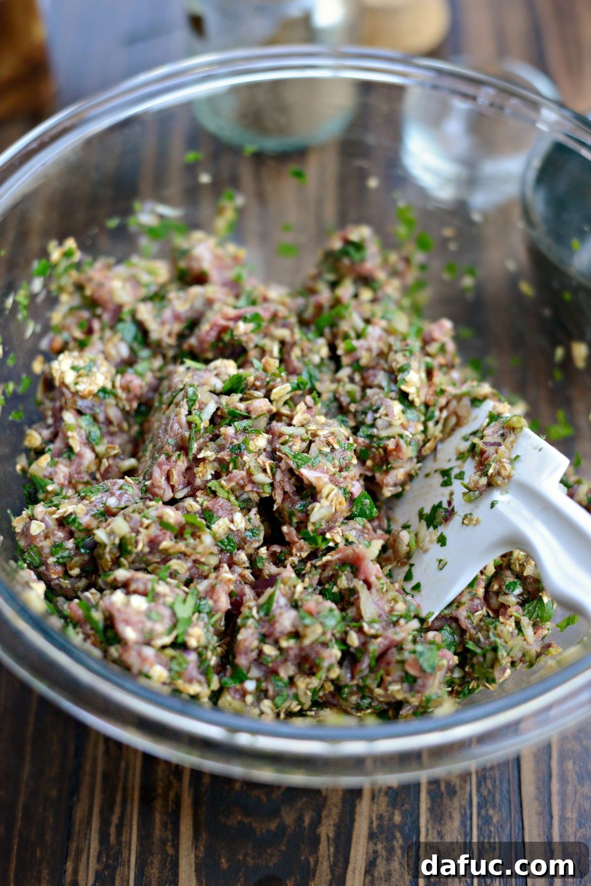 The lamb meatball mixture being thoroughly mixed in a bowl with a fork and spatula.
