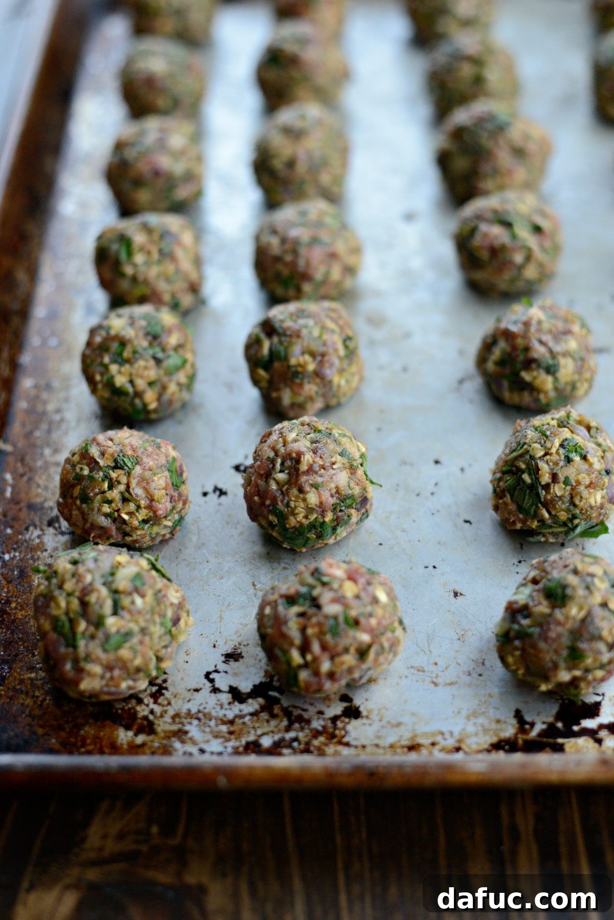 A hand rolling the spiced lamb mixture into uniform meatballs.