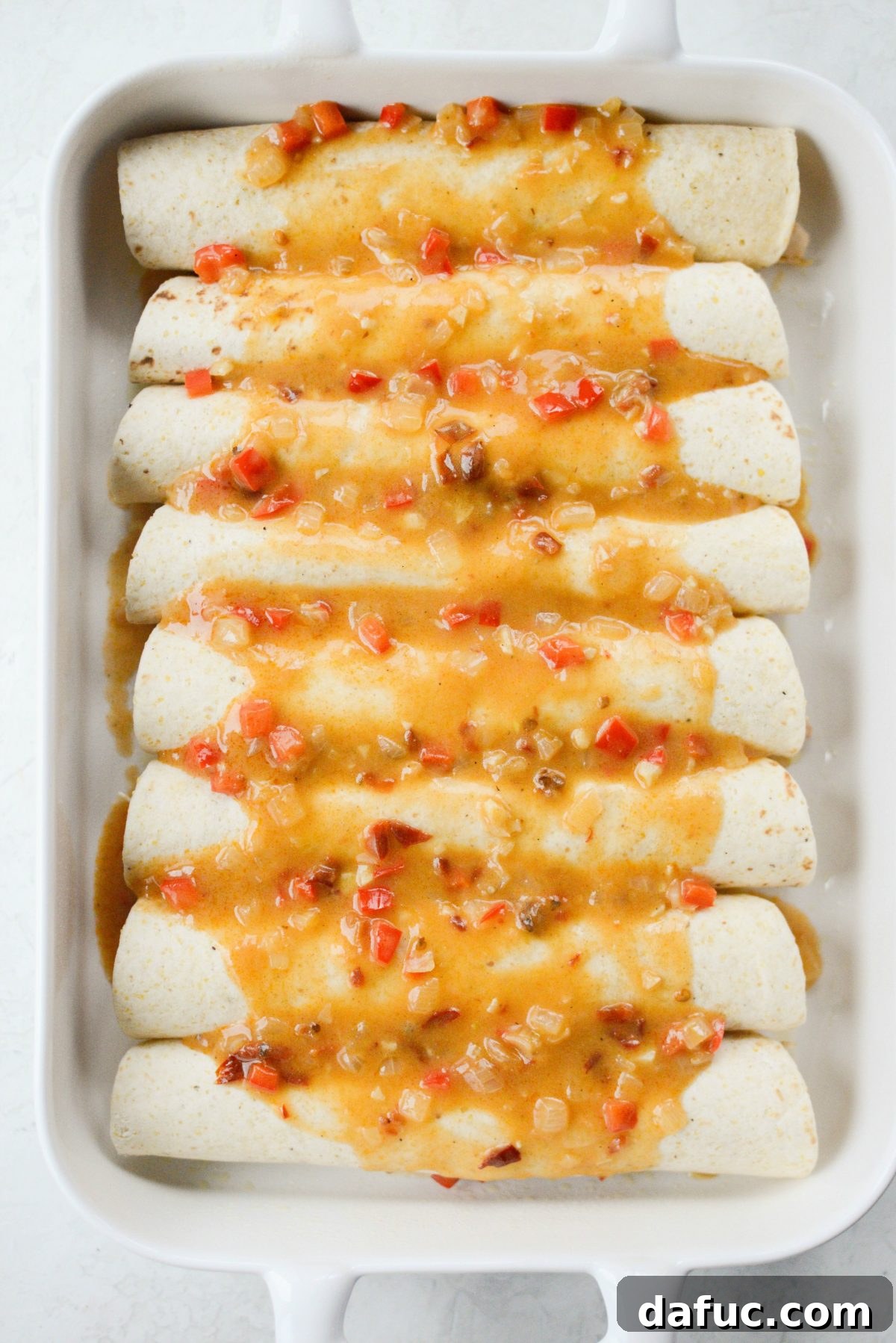 Pouring the remaining chipotle sauce over the rolled enchiladas