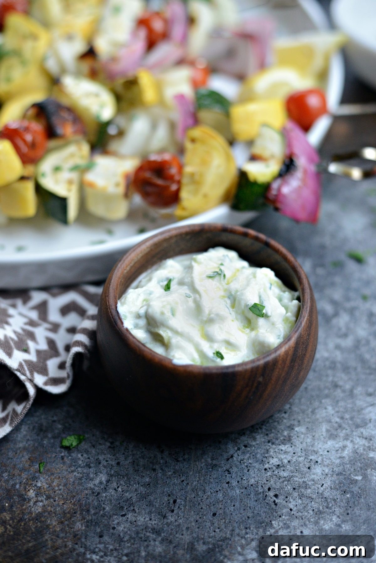 Creamy Homemade Tzatziki 8 Homemade Tzatziki - A bowl of fresh homemade tzatziki on a wooden surface, with a spoon ready for serving.