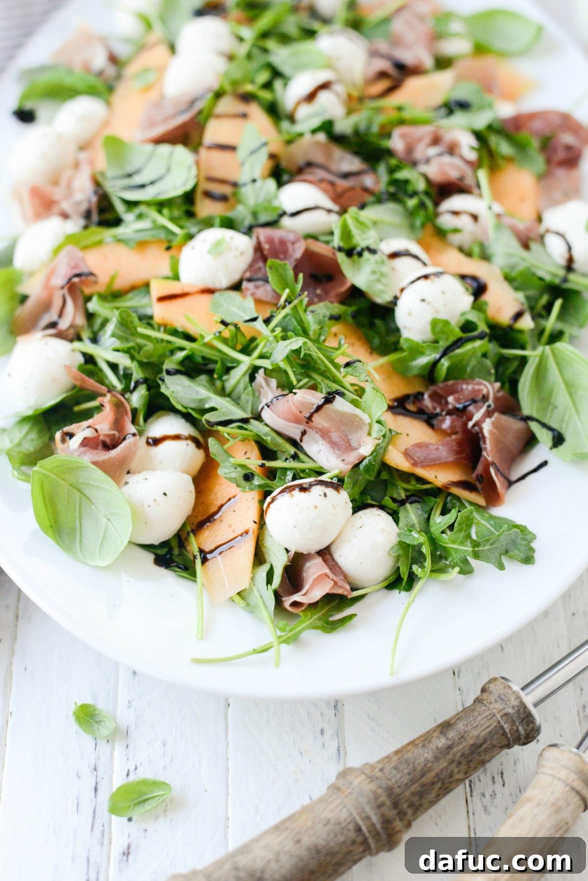 Golden Melon Prosciutto Arugula Fresca 8 Finished Cantaloupe and Prosciutto Arugula Caprese Salad on a platter, garnished with basil and balsamic glaze