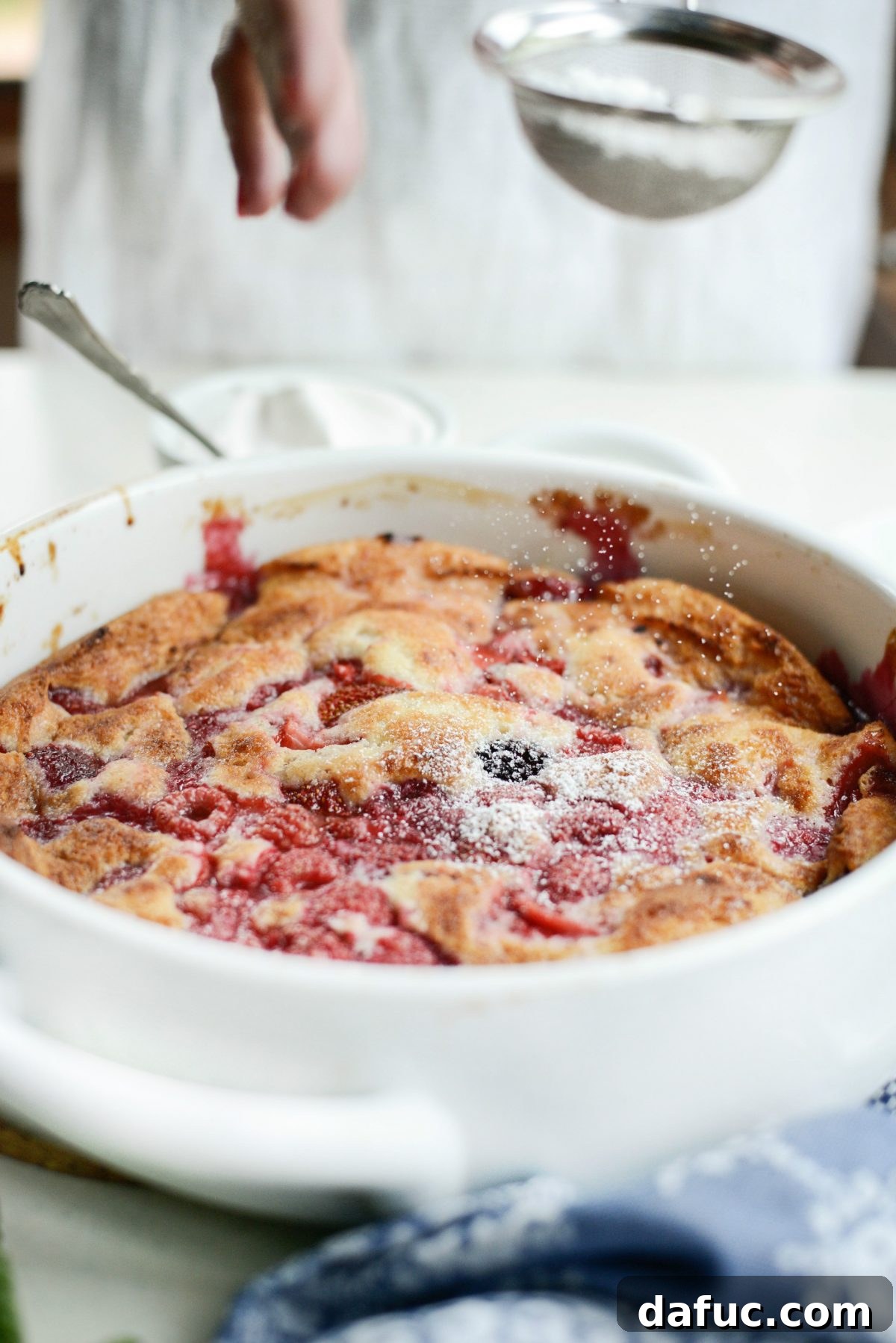 Triple Berry Cobbler being dusted with powdered sugar.
