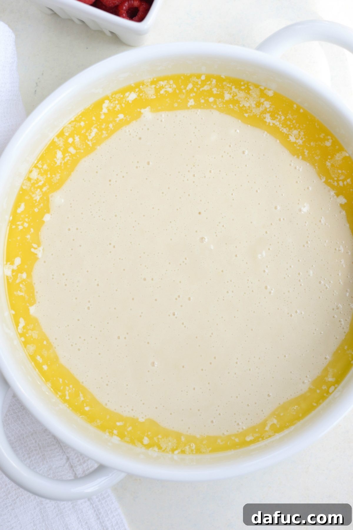 Pouring cobbler batter over melted butter in a baking dish.