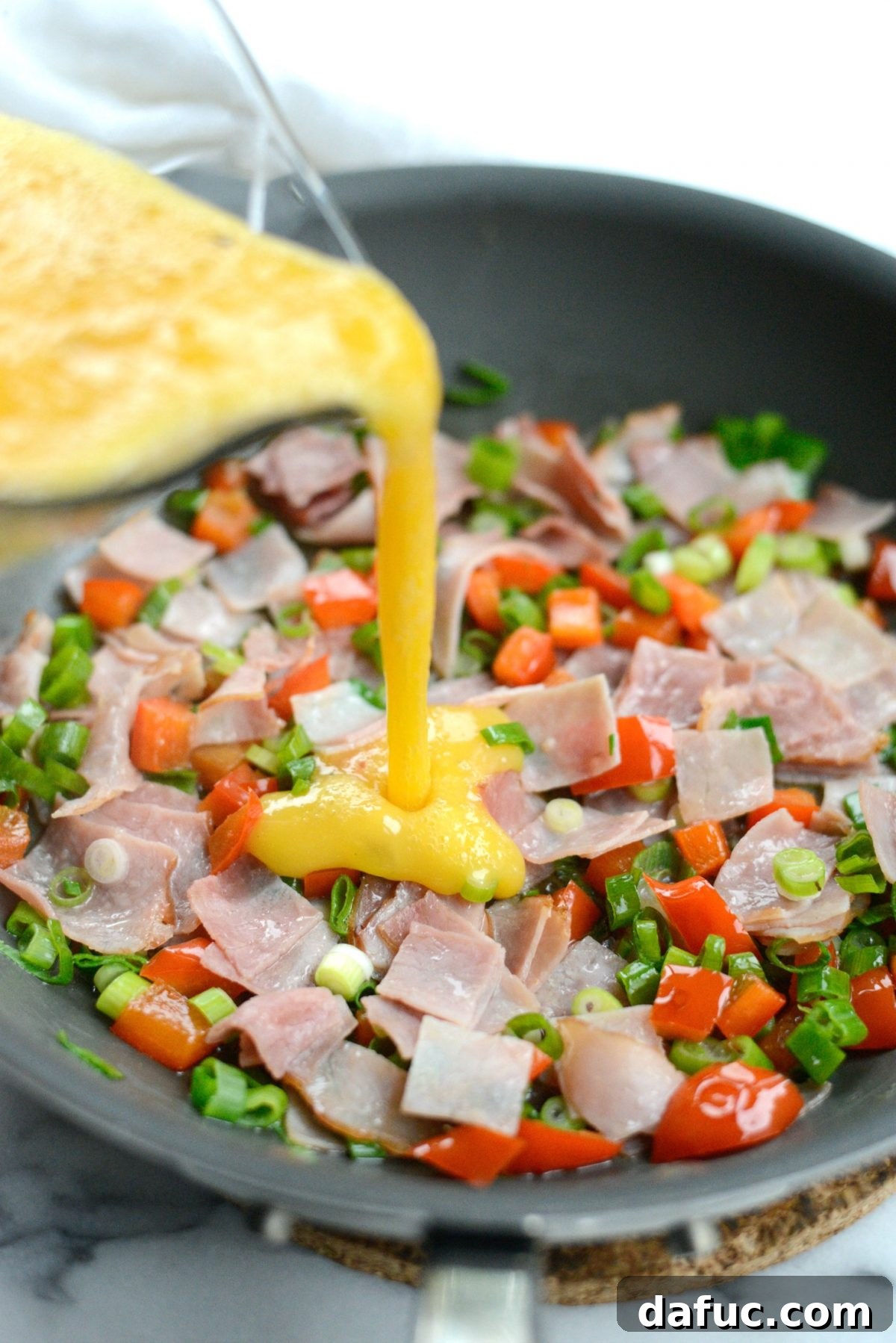 Cowboy Breakfast Frittata 7 Whisked eggs being poured over the sautéed ham and pepper mixture in a skillet