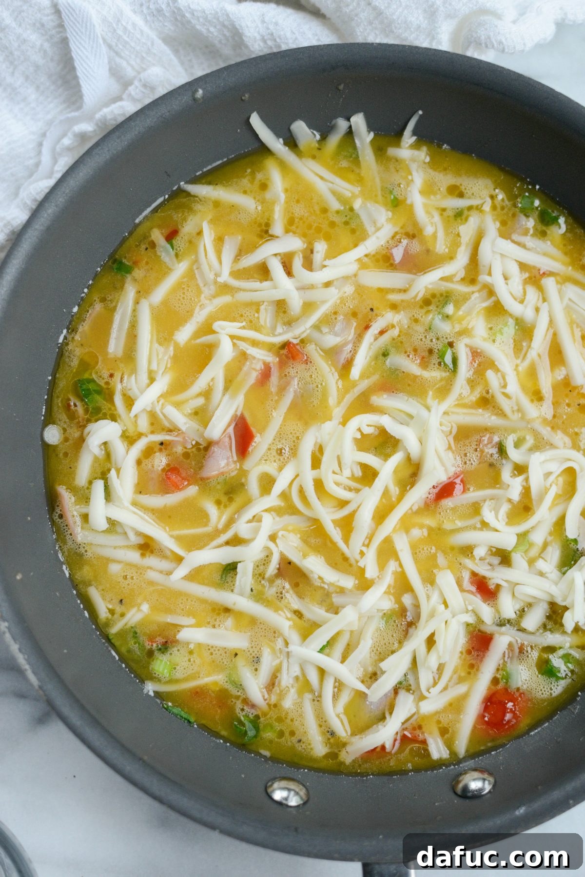 Cowboy Breakfast Frittata 8 Shredded Swiss cheese sprinkled generously over the poured eggs and ham in the skillet
