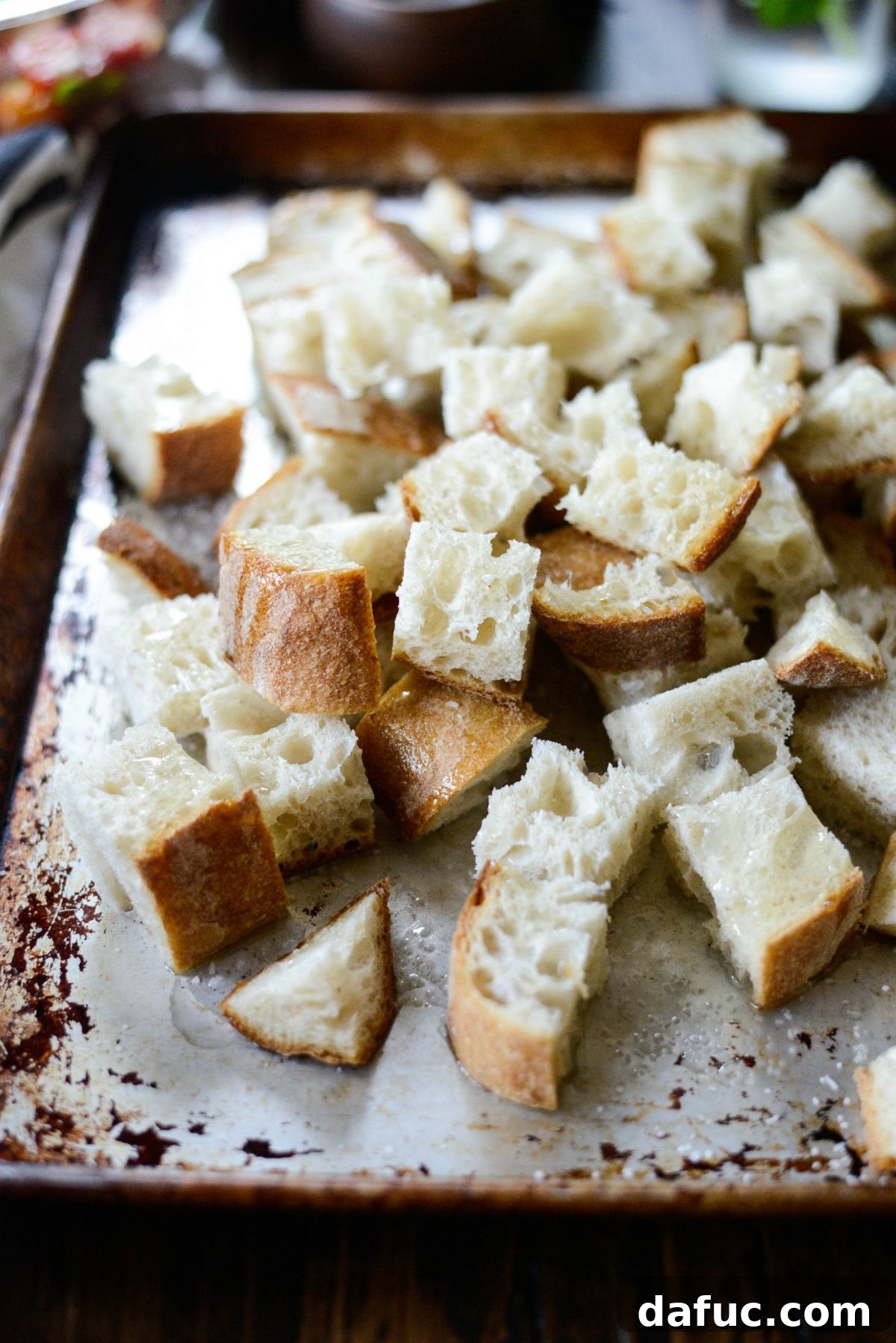 Cubed crusty bread spread on a rimmed baking sheet, ready for toasting