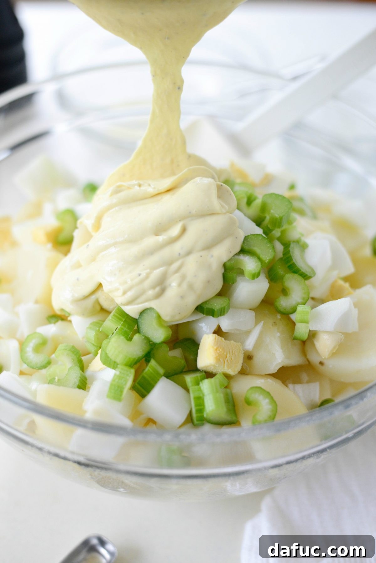The prepared dressing being poured over the potato salad mixture.