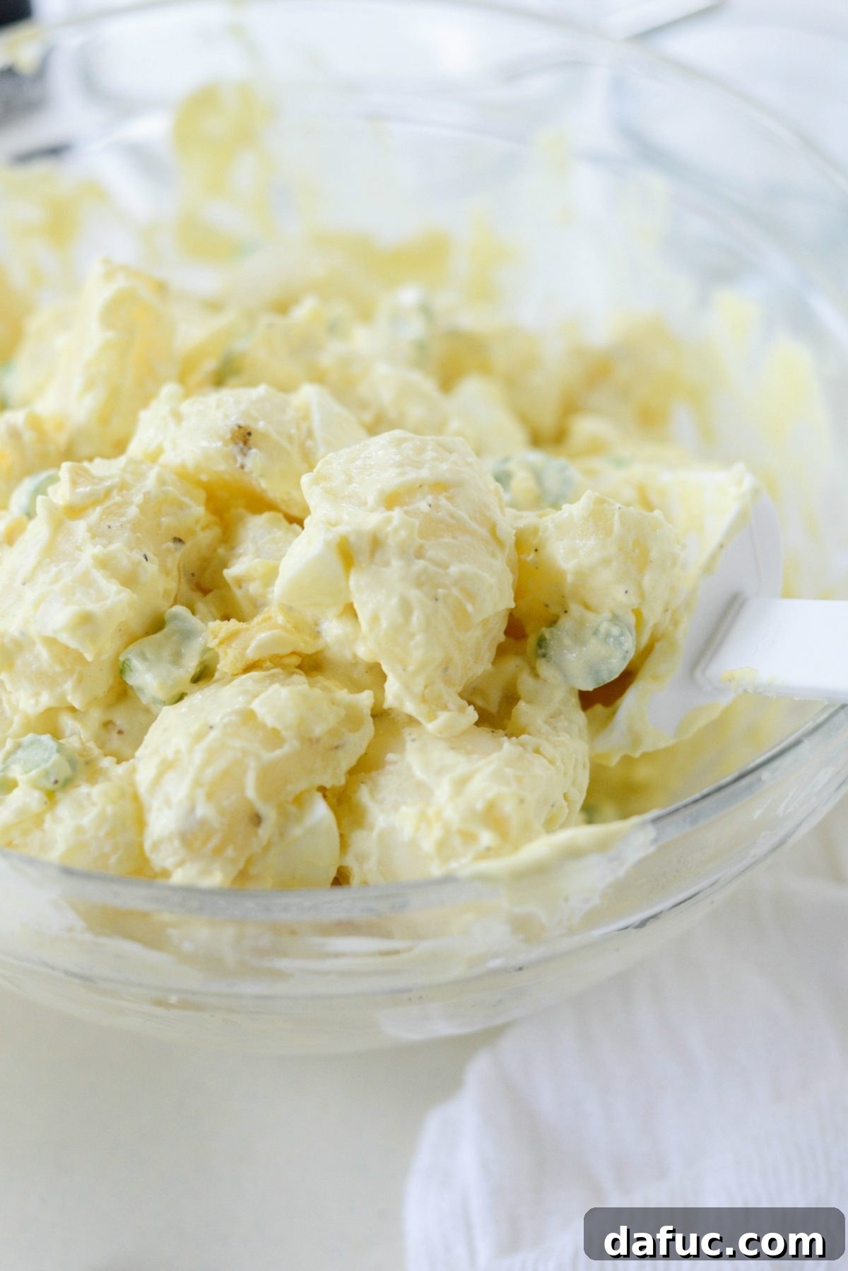 Potato salad being tossed gently to combine all ingredients with the dressing.