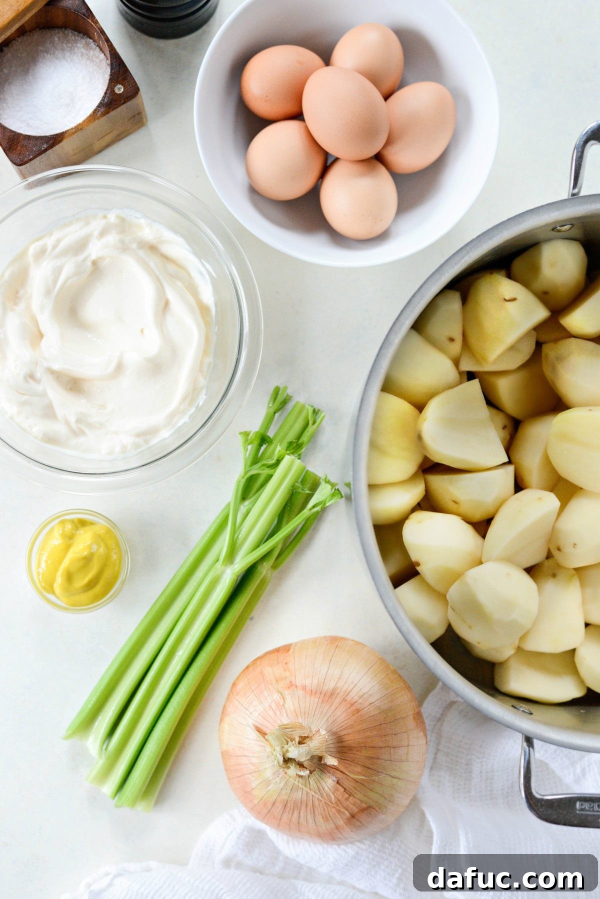 Ingredients laid out for Aunt Penny's Classic Potato Salad Recipe, including potatoes, mayonnaise, mustard, and fresh vegetables.