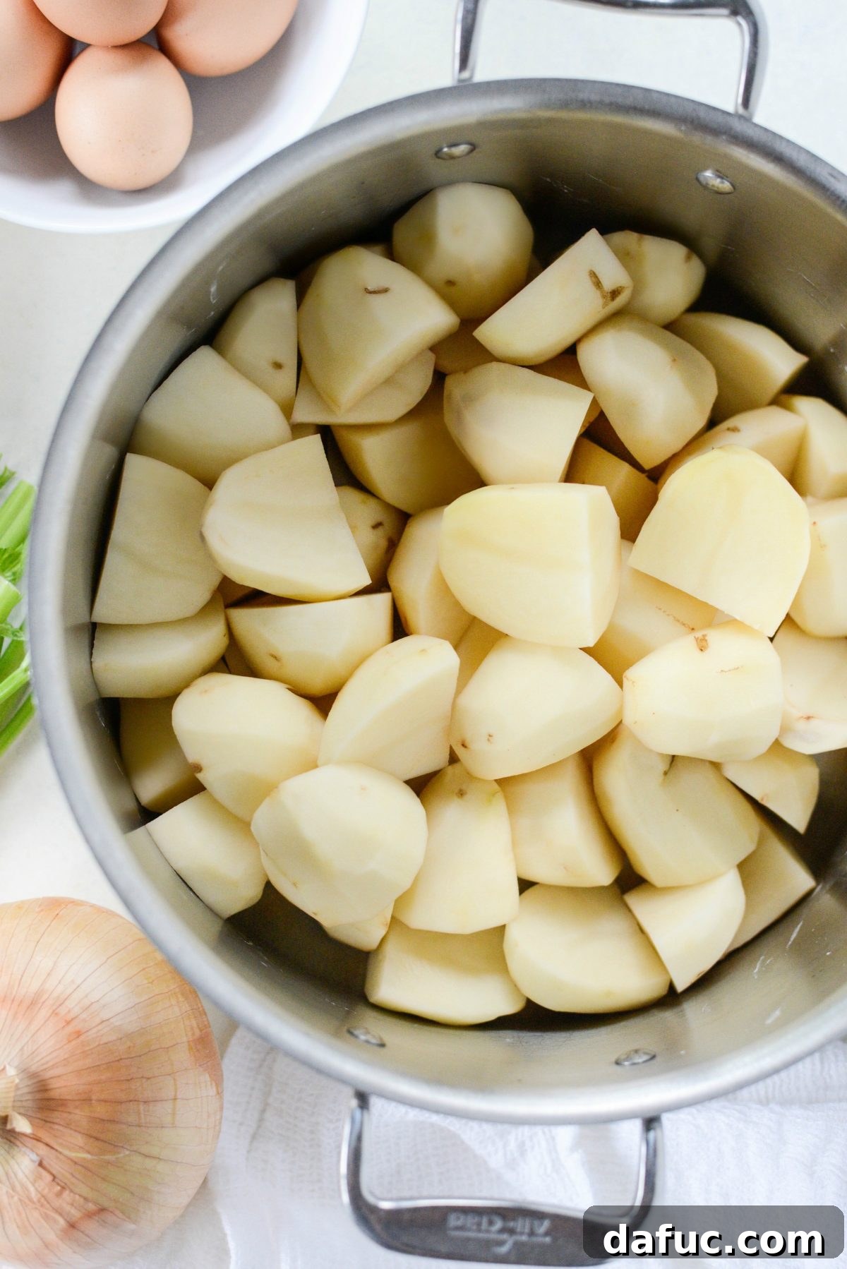 Peeled and chopped russet potatoes being added to a large pot for cooking.