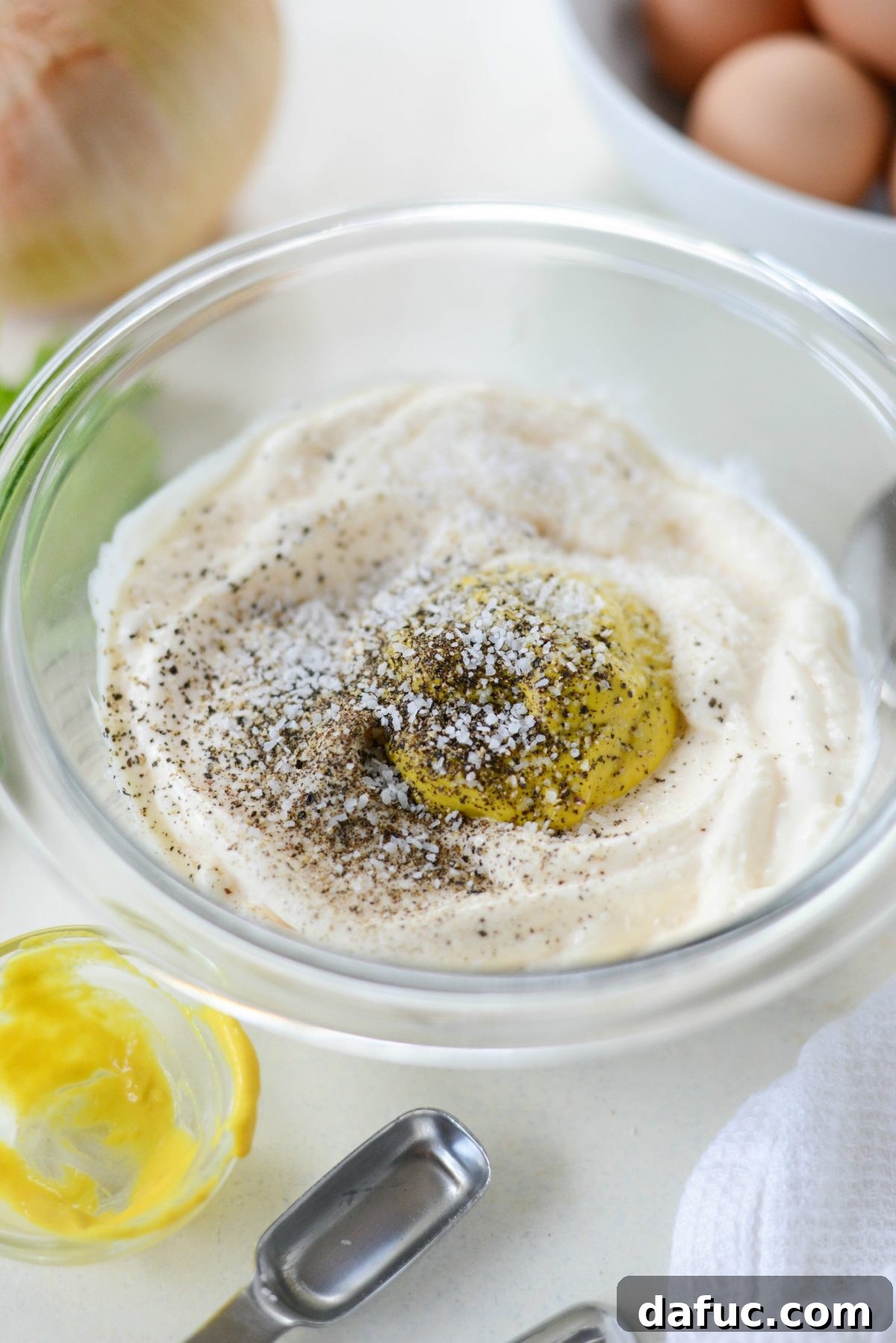 Ingredients for the potato salad dressing, including mayonnaise, mustard, salt, and pepper, in a bowl.