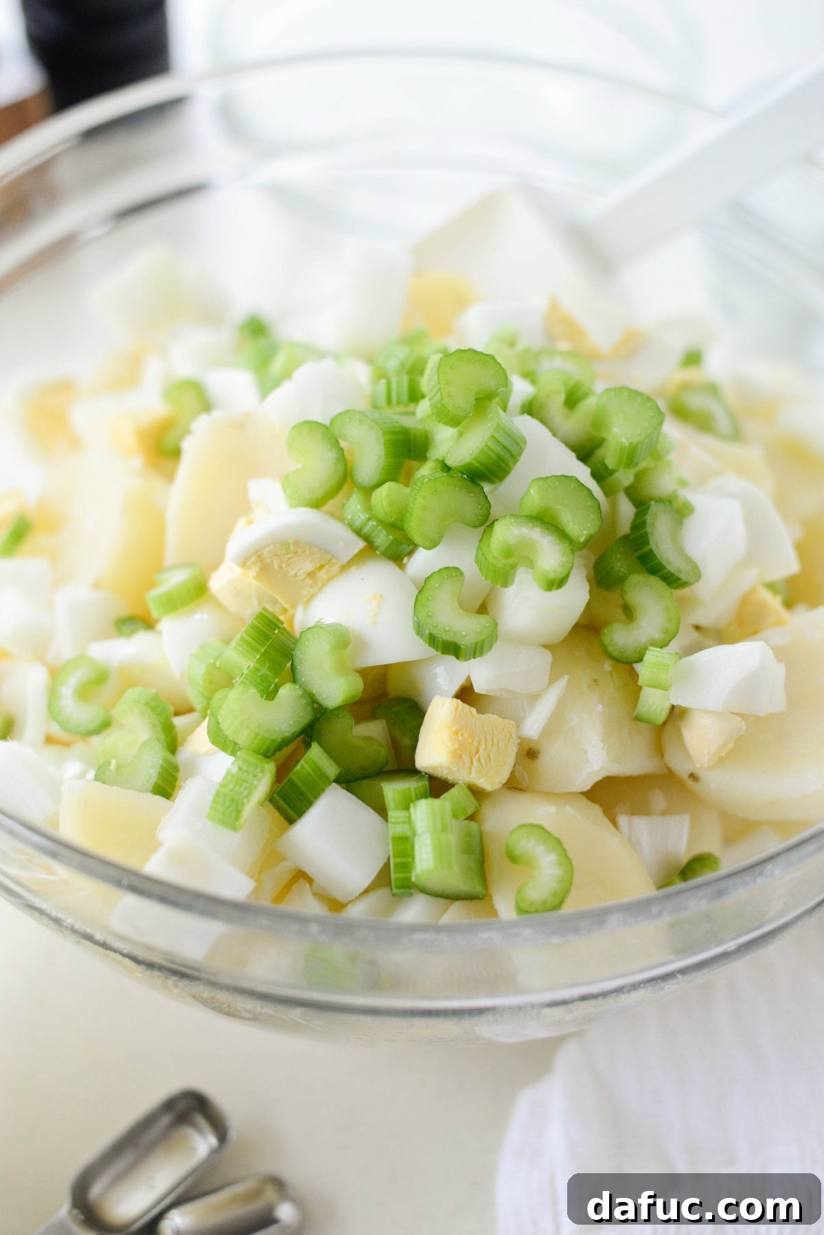 Cooled potatoes with chopped hard-boiled eggs, onion, and celery added to the bowl.