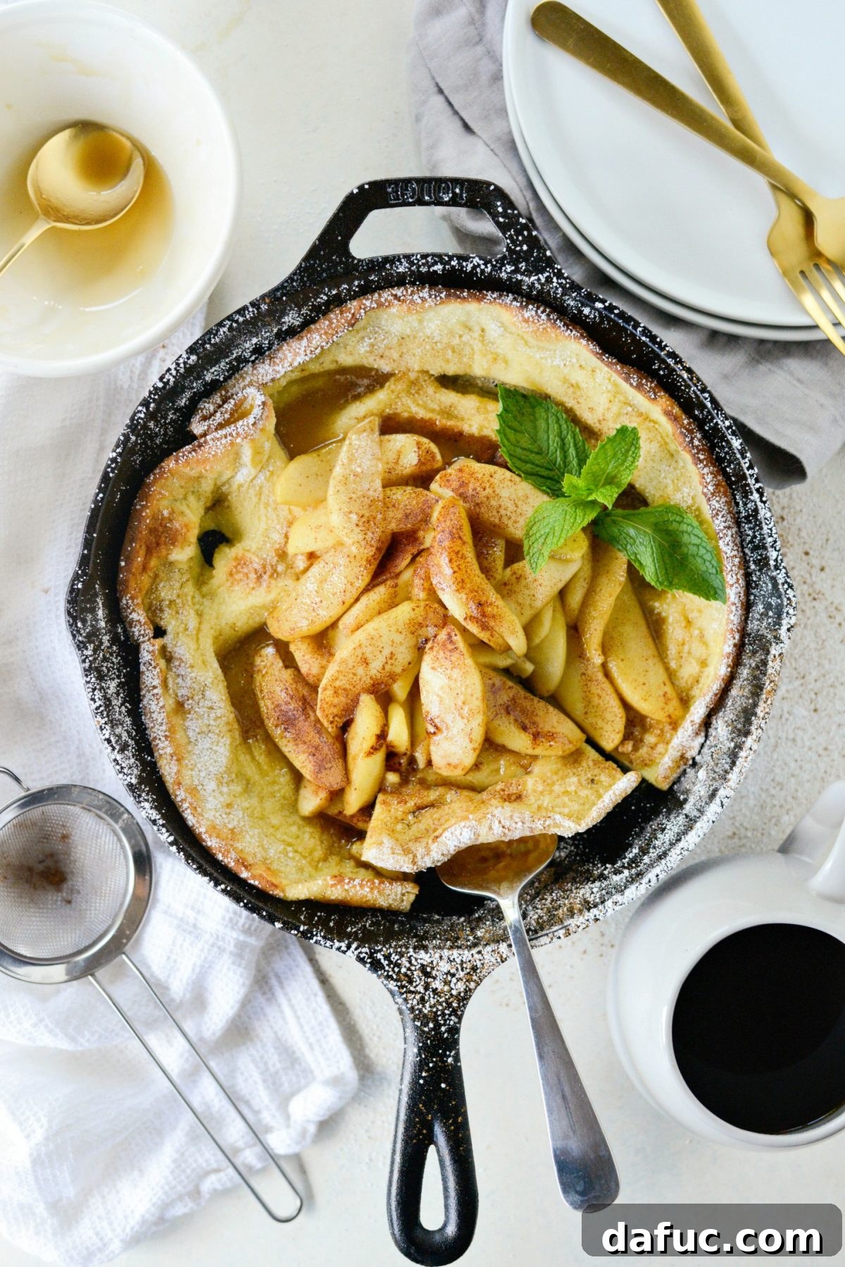 Sweet Caramel Apple Skillet Puff 2 Golden Caramelized Apple Dutch Baby in a cast iron skillet, dusted with powdered sugar and cinnamon.
