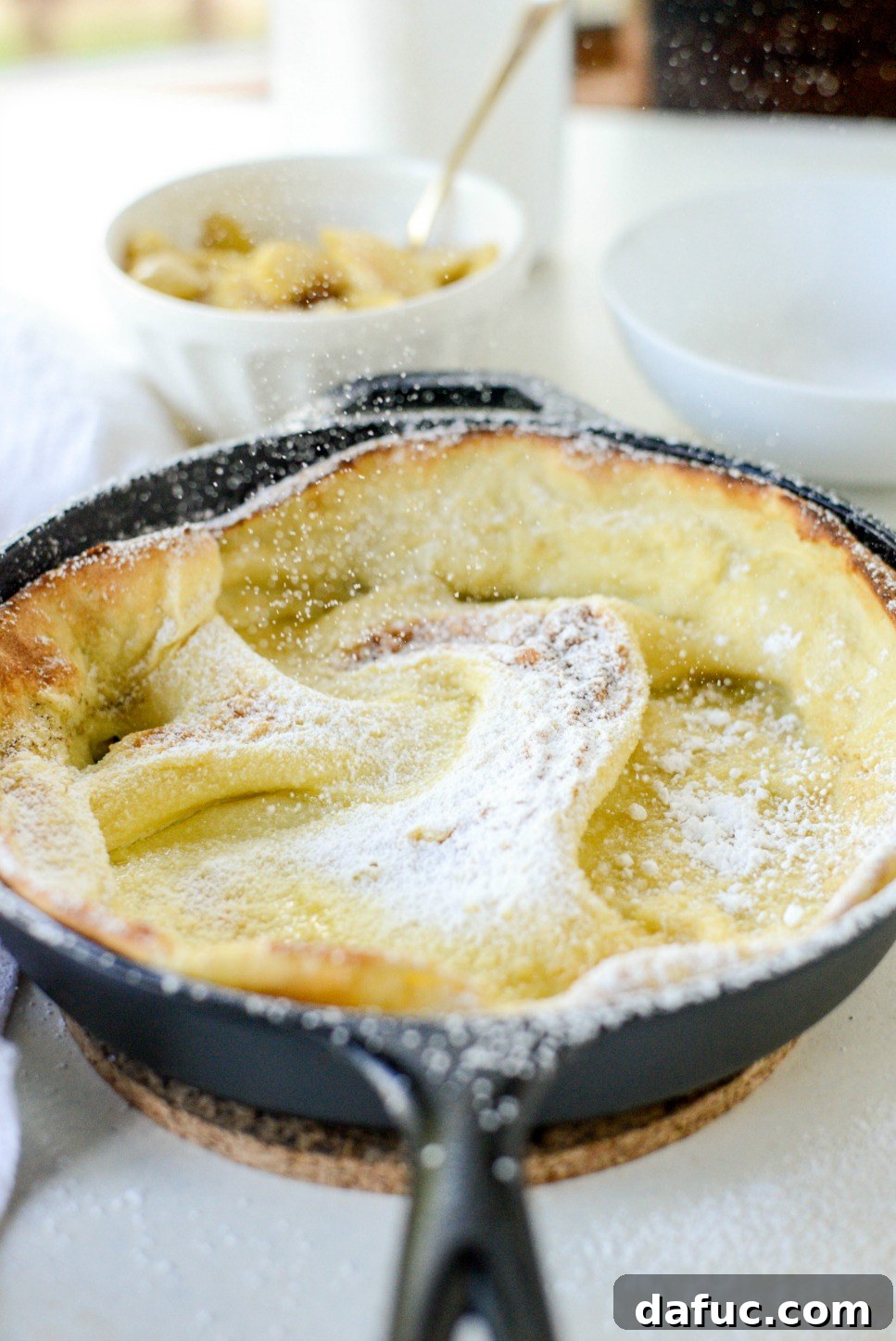 Sweet Caramel Apple Skillet Puff 11 Freshly baked Dutch Baby, slightly deflated, being dusted with powdered sugar.