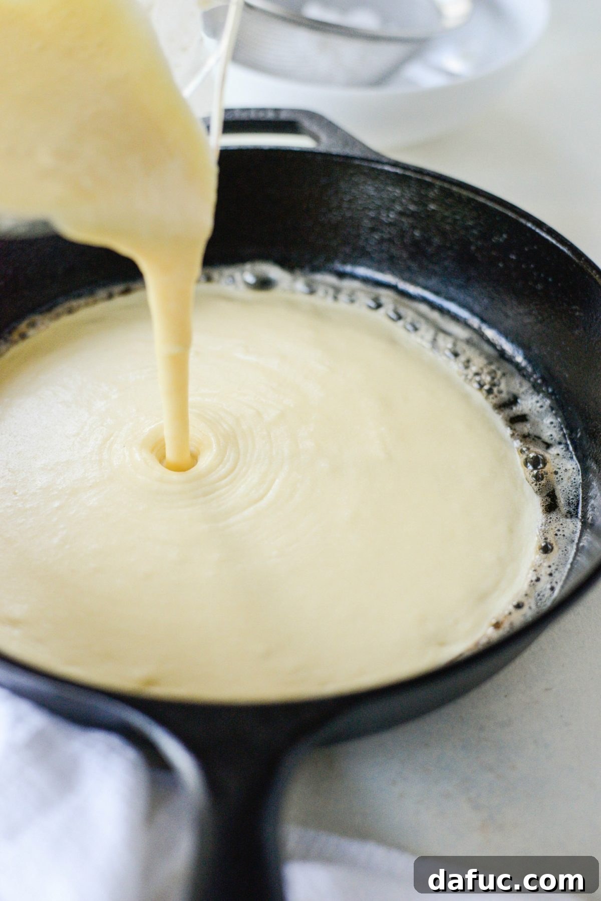 Sweet Caramel Apple Skillet Puff 9 Pouring Dutch Baby batter into a hot cast iron skillet.