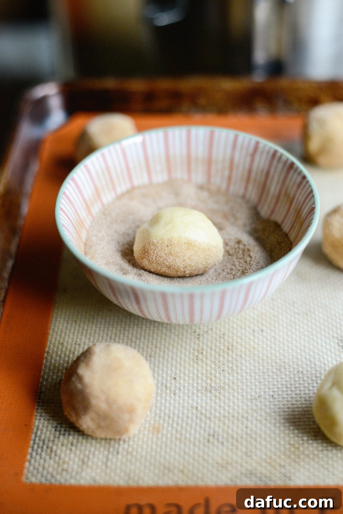 Golden Cinnamon Sugar Delights 12 A cookie dough ball being rolled in cinnamon sugar to coat it evenly.