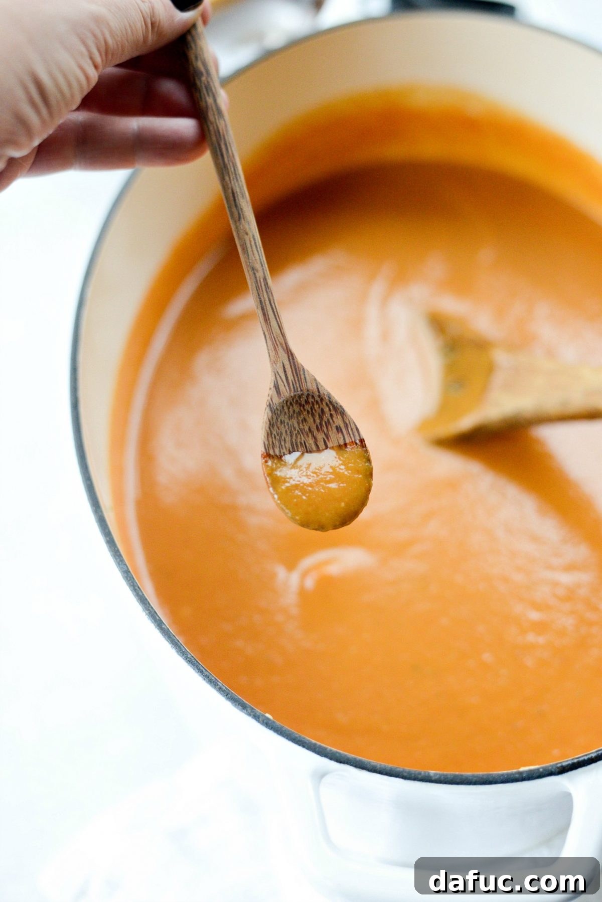 Spoonful of Roasted Tomato Pumpkin Soup being tasted for seasoning, with salt and pepper shakers in the background