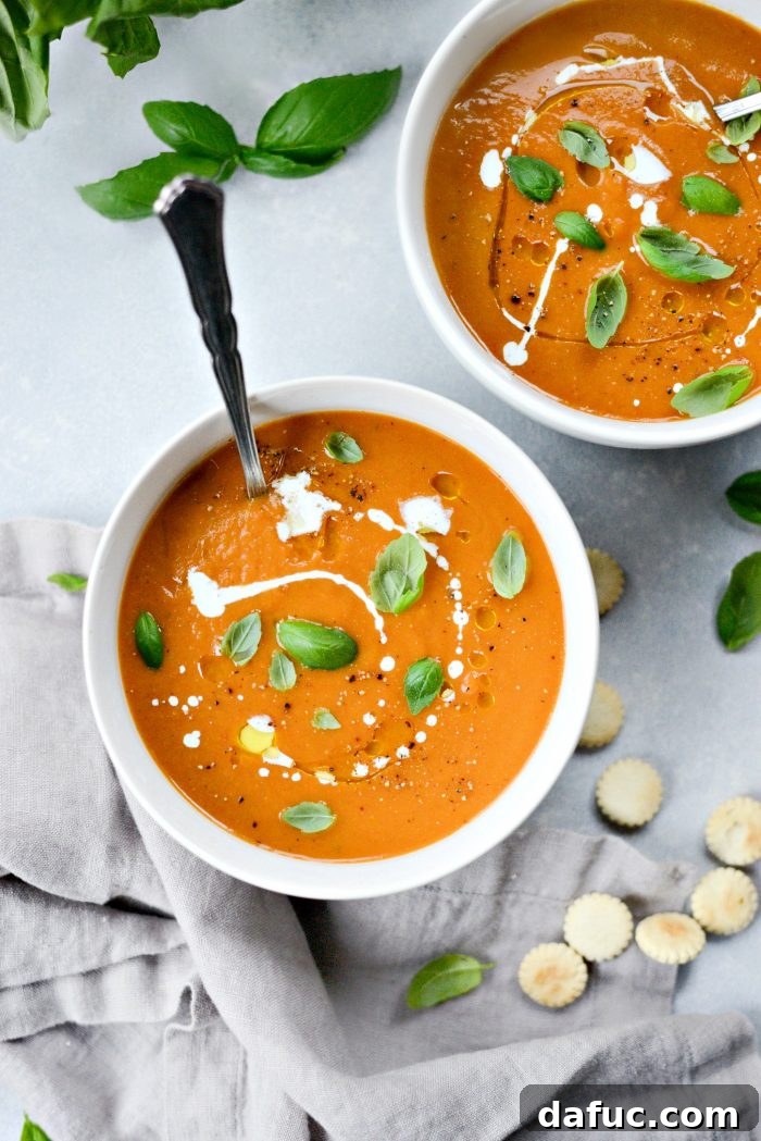 A bowl of creamy Roasted Tomato Pumpkin Soup drizzled with olive oil and heavy cream, garnished with fresh basil and served with soup crackers