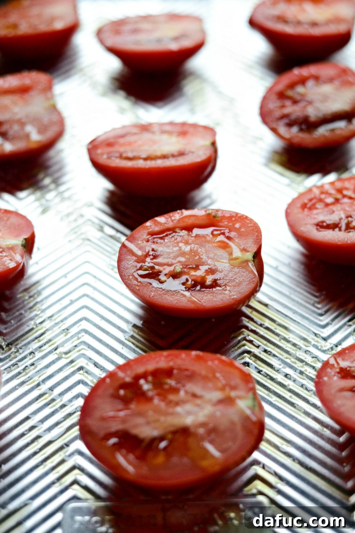 Halved Roma tomatoes drizzled with olive oil and seasoned with salt, arranged cut-side up on a rimmed baking sheet, ready for roasting