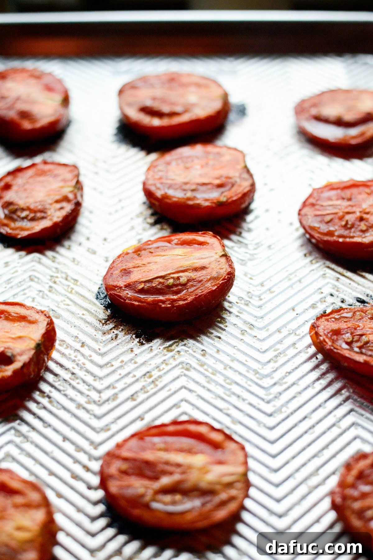 Close-up of perfectly roasted Roma tomatoes on a baking sheet, with softened edges and concentrated flavor