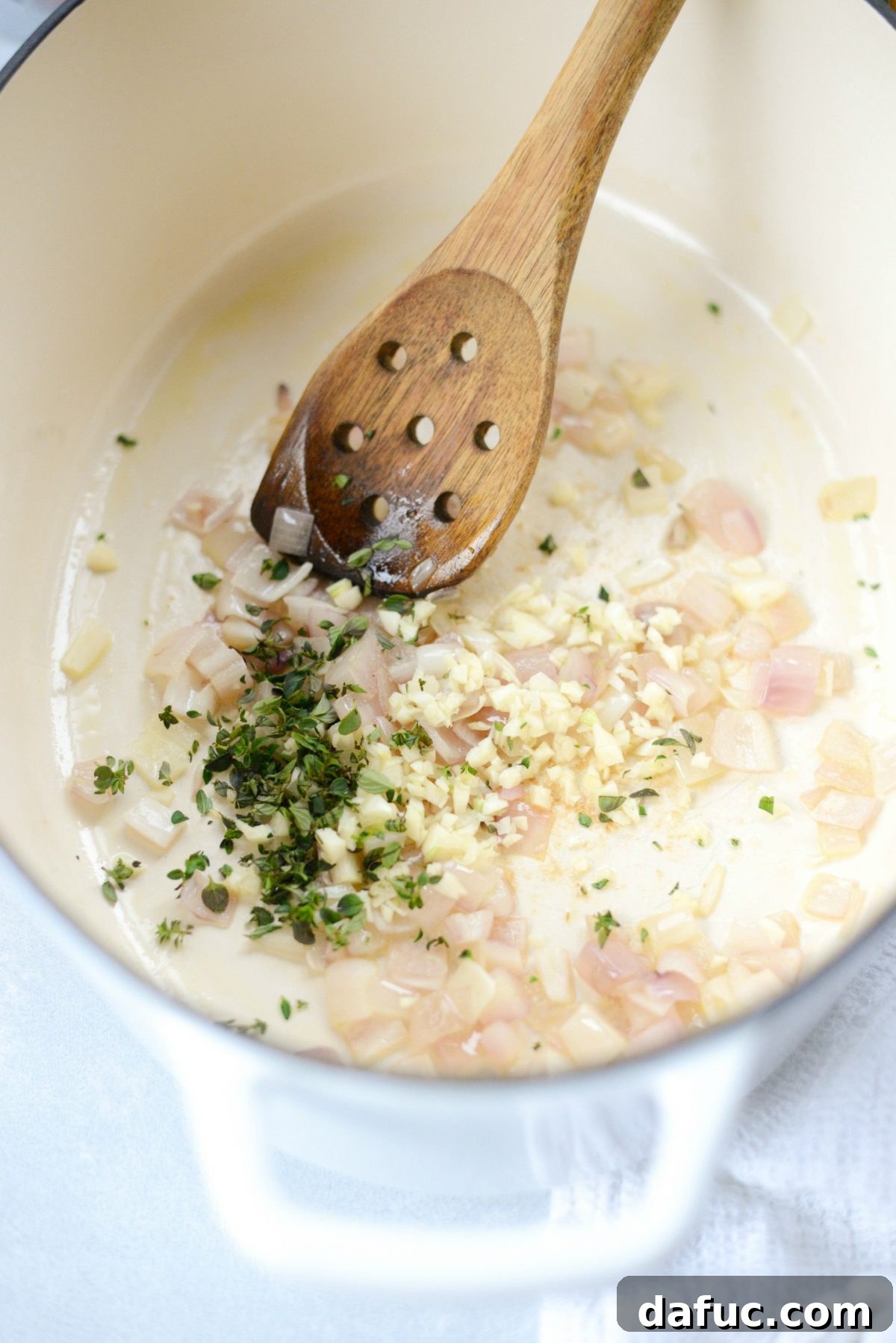 Diced shallots gently sautéing in olive oil in a pan, becoming soft and translucent