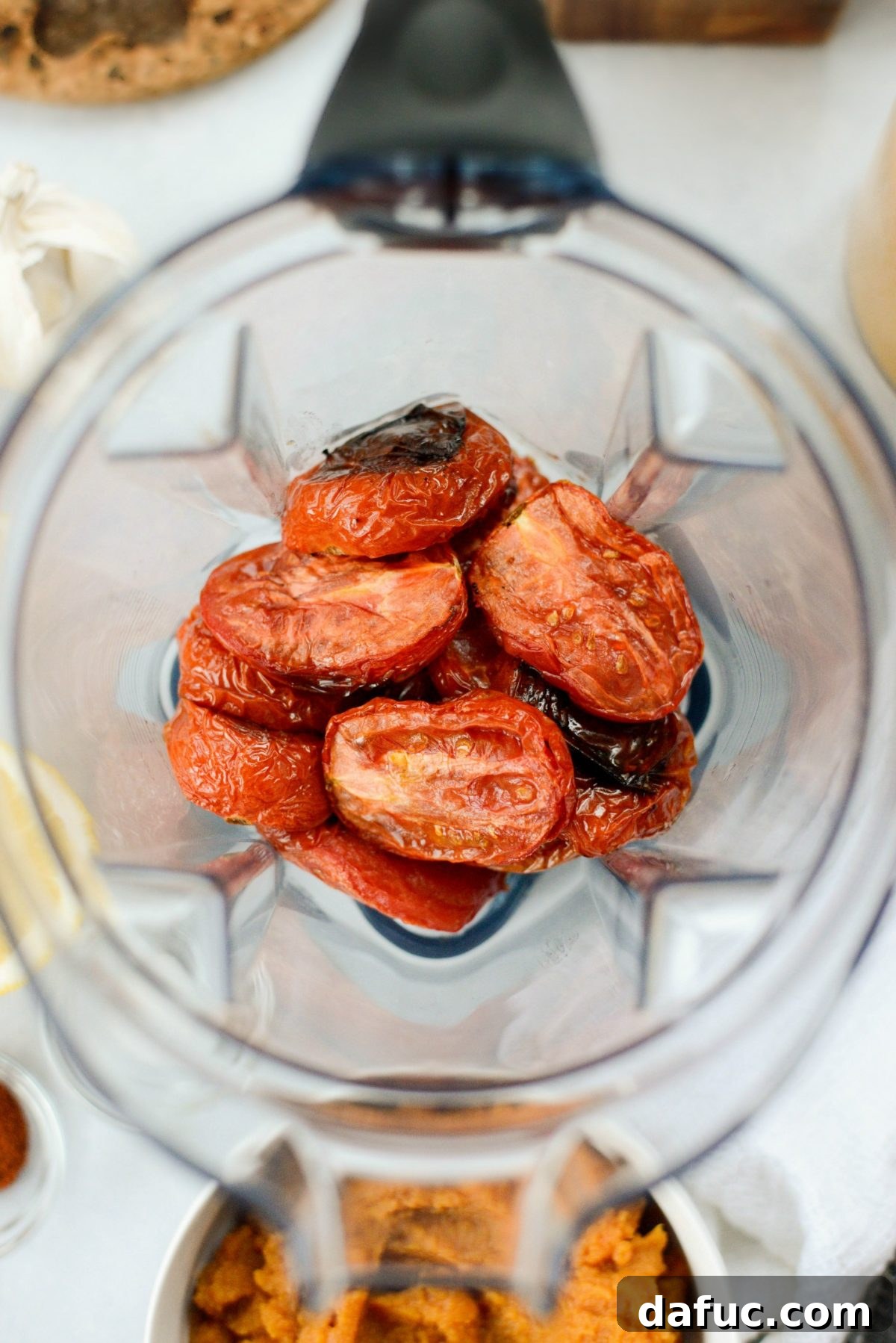 Roasted tomatoes being transferred into a blender, ready for the next step of making soup