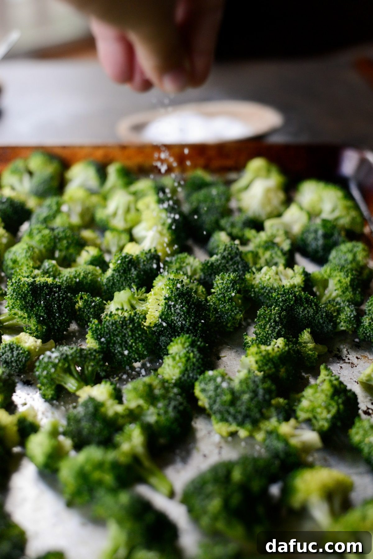 Broccoli florets on a baking sheet, generously seasoned with kosher salt before roasting.