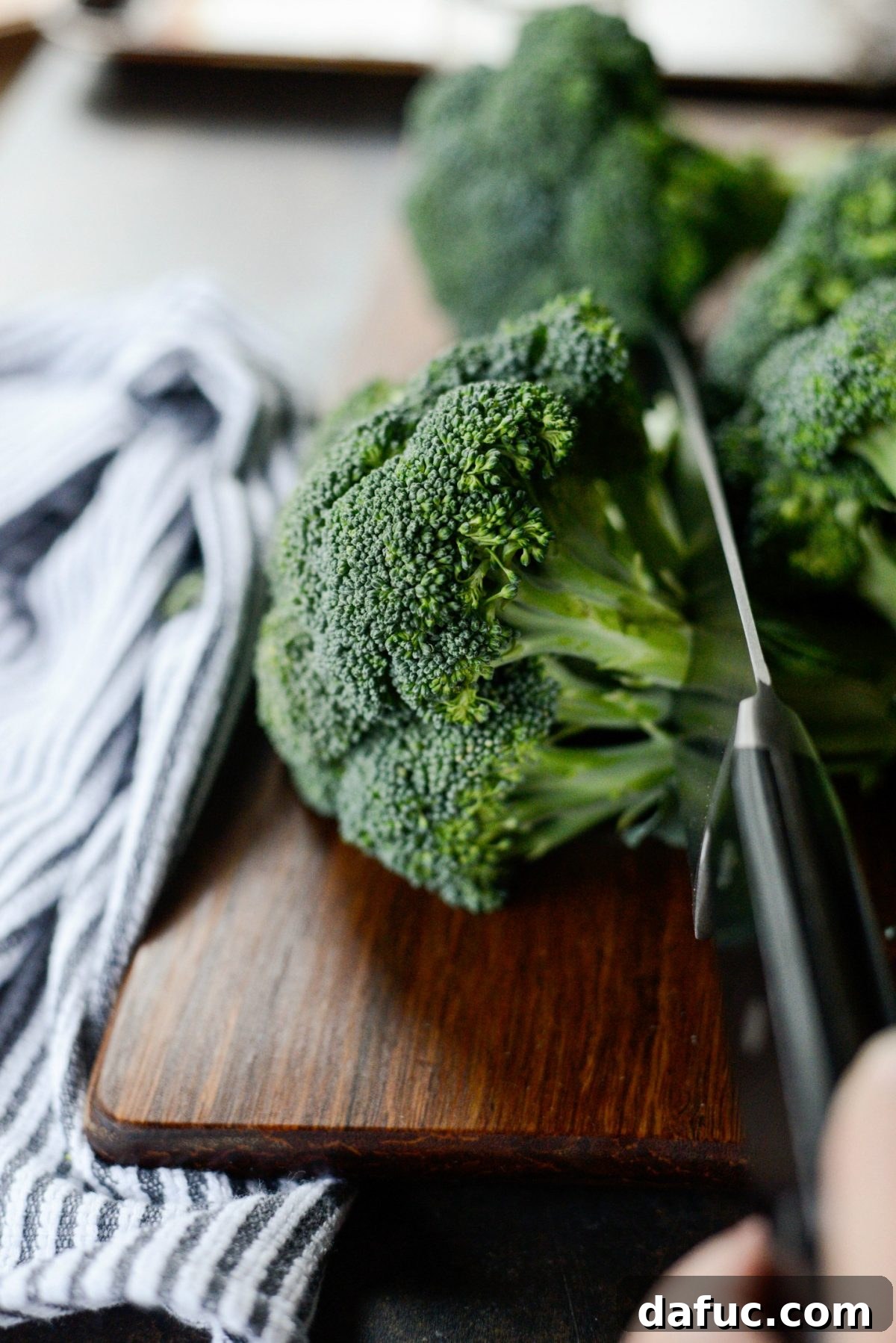 Trim broccoli into florets - Hands trimming a head of broccoli into small, bite-sized florets on a cutting board.