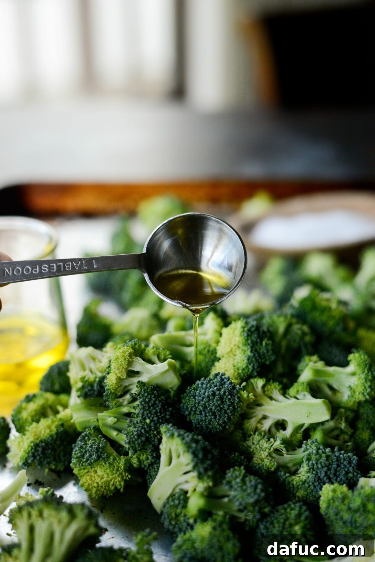 Drizzling extra light olive oil over broccoli florets on a baking sheet.