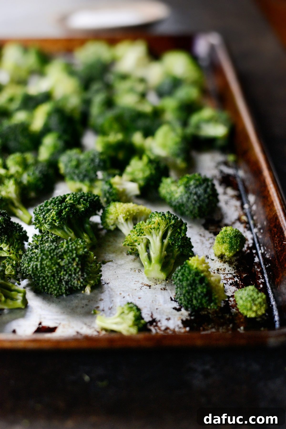 Broccoli florets spread in a single, even layer on a baking sheet, with flat sides down.