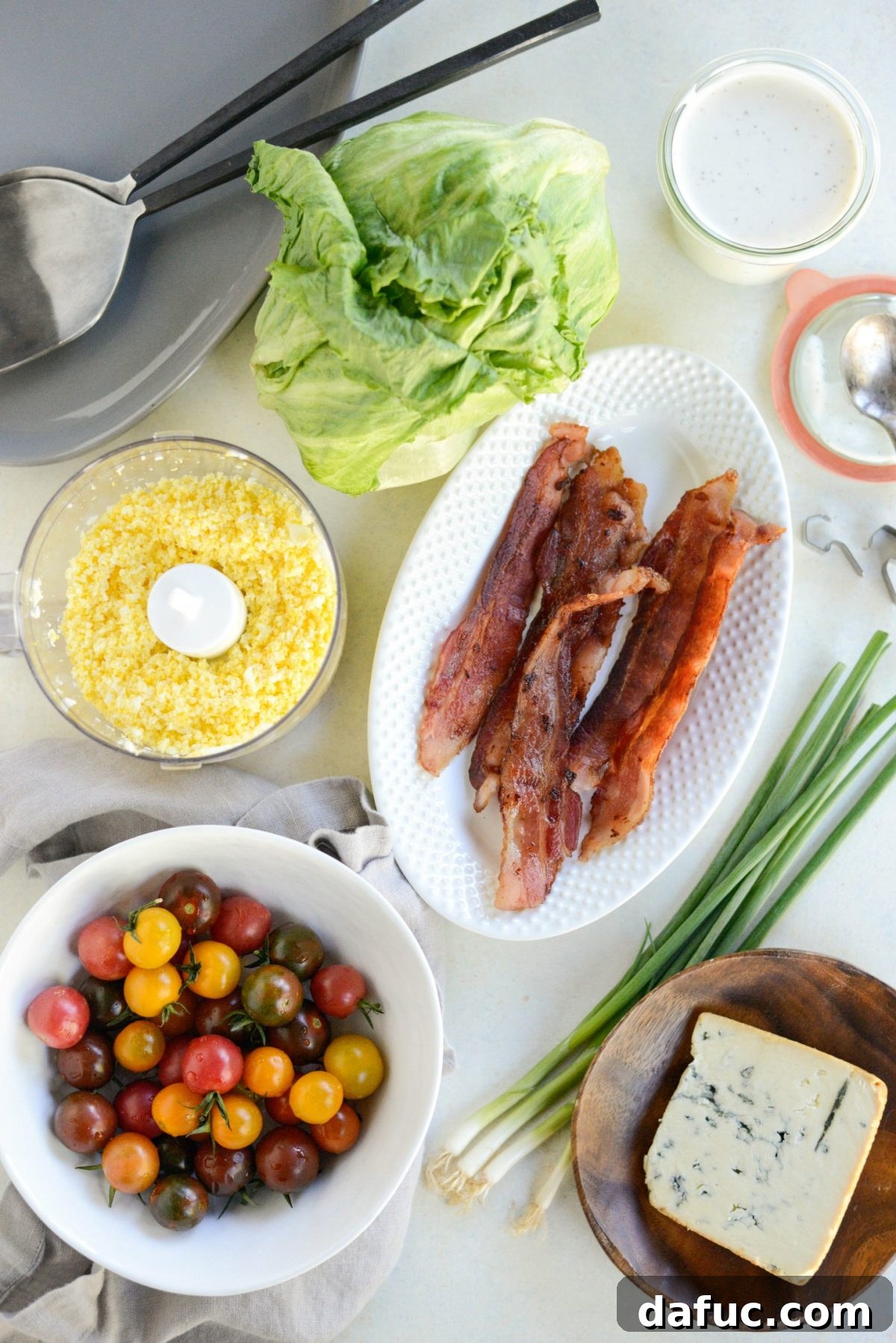 Our Signature Loaded Wedge, Drenched in Peppercorn Buttermilk 4 All the fresh ingredients laid out for making the Loaded Wedge Salad, including iceberg lettuce, tomatoes, blue cheese, hardboiled eggs, bacon, and dressing components.
